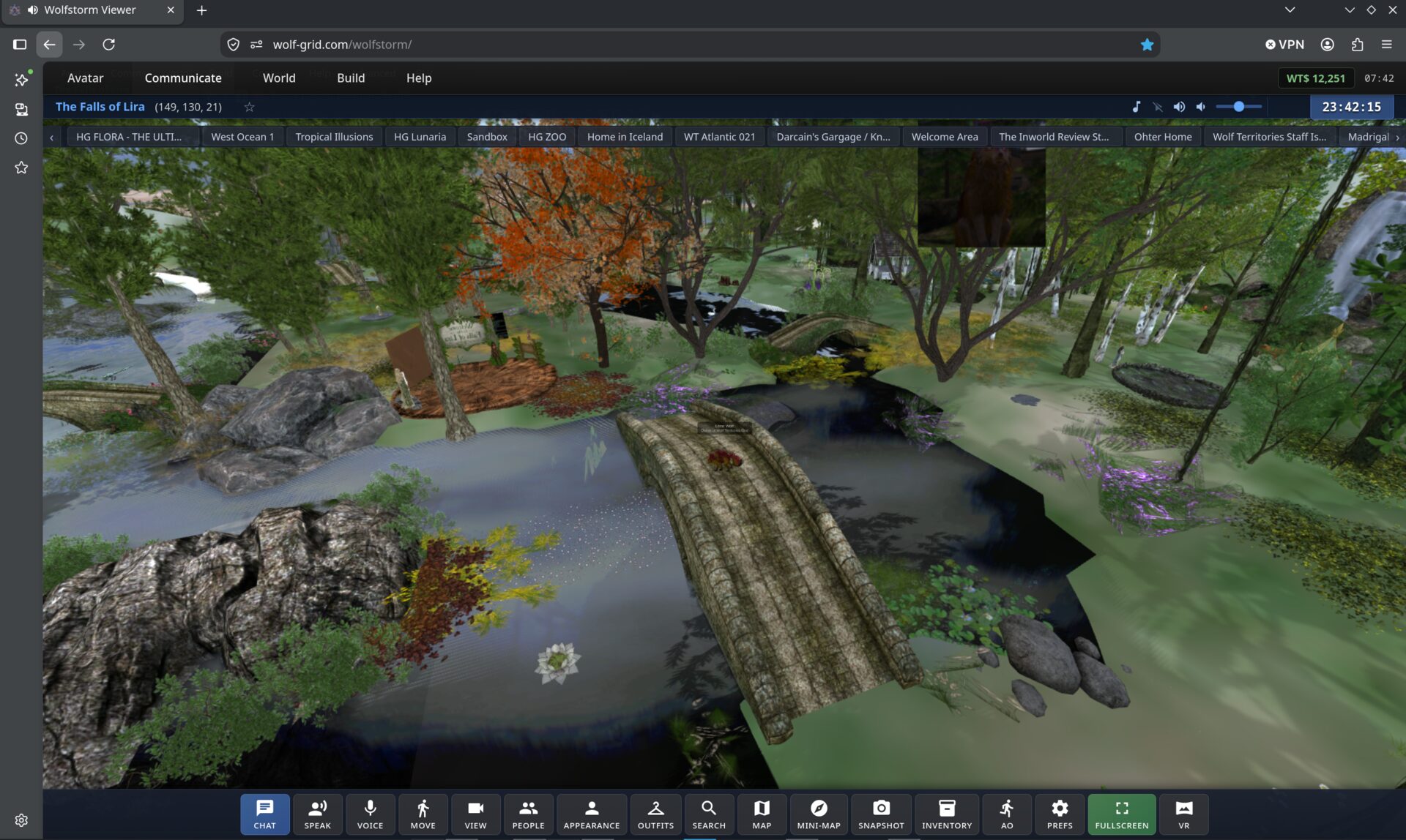 WolfStorm open in a Chrome tab at wolfstorm.app. The region The Falls of Lira fills the window: a stone bridge crossing a river between autumn trees and mossy rocks. Menus for Avatar, Communicate, World, Build and Help run along the top, a row of saved region tabs sits beneath them, and a toolbar of chat, voice, movement, appearance, map, inventory, fullscreen and VR buttons runs along the bottom.